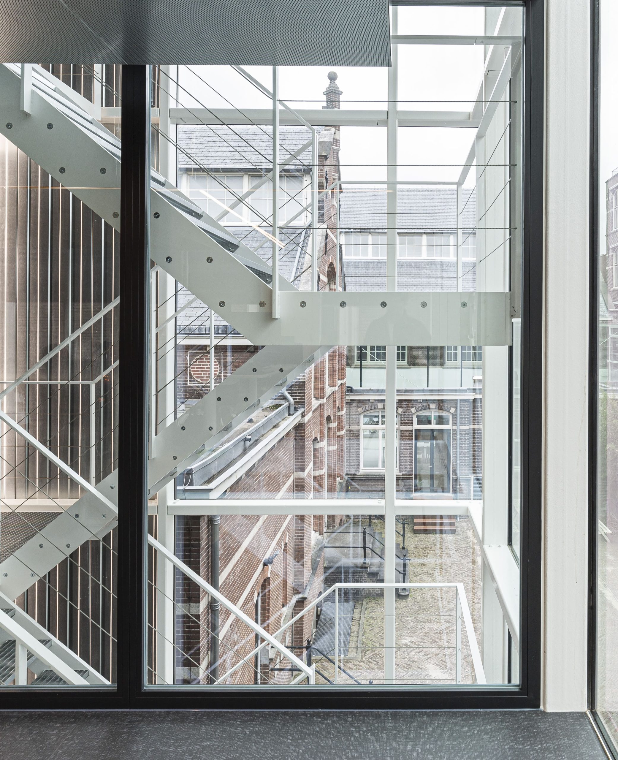 Blick aus dem Fenster auf eine weiße Außentreppe aus Metall, dahinter mehrere Backsteingebäude. Building D(emountable), Foto: Lucas van der Wee