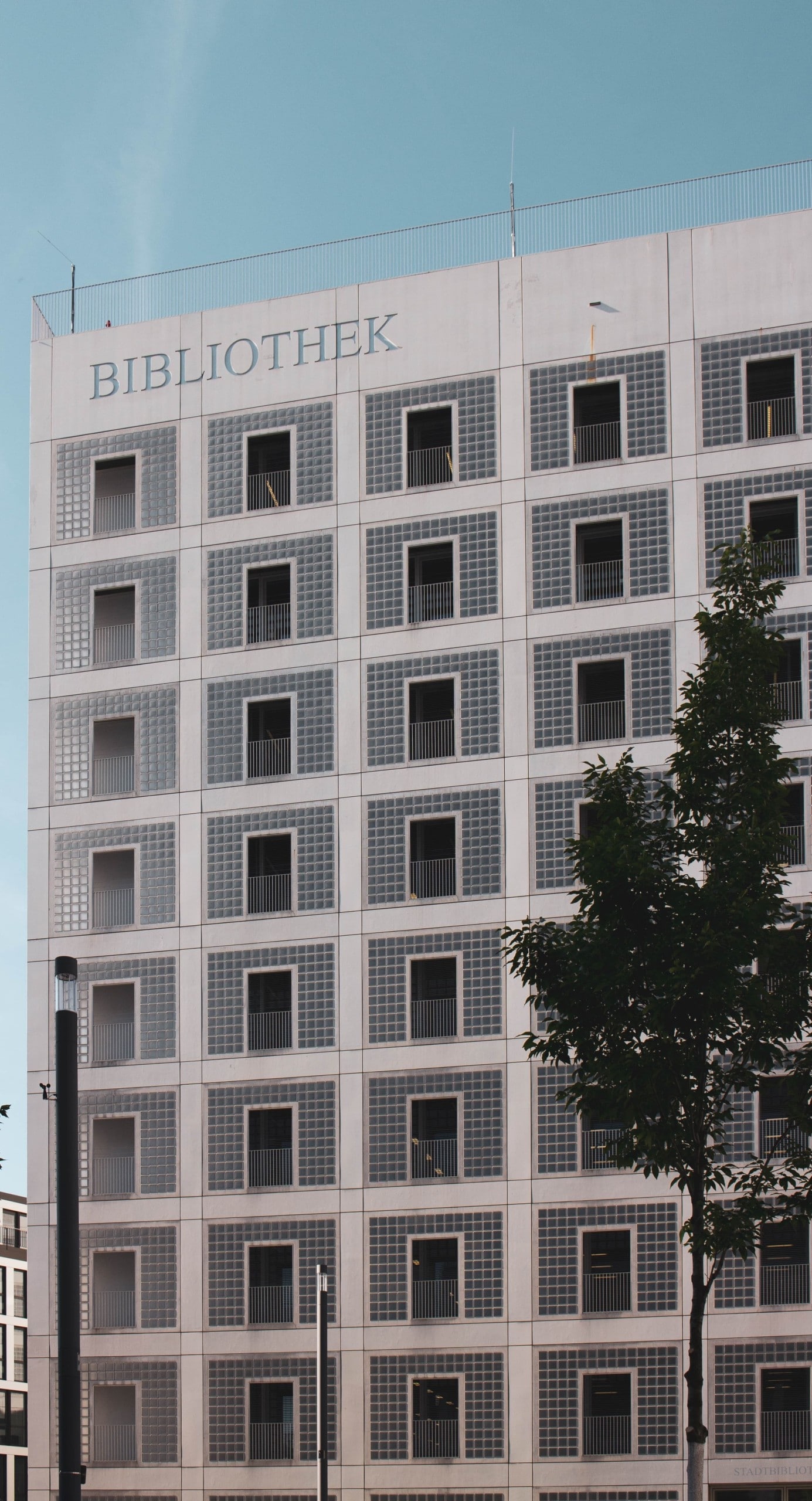 Blick auf die Fassade eines Gebäudes mit gerasterter Fassade, dessen Flächen mit Glasbausteinen gefüllt sind. Stadtbibliothek Stuttgart, Foto: Marcel Strauß via Unsplash