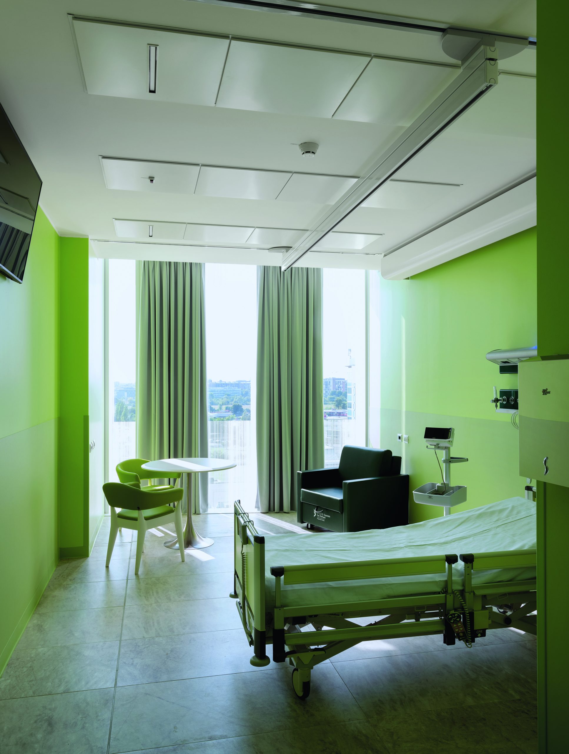 Patientenzimmer in einem Krankenhaus, Wände und Einrichtung sind hellgrün, bodentiefe Fenster lassen Licht in den Raum. Mario Cucinella Architects, Ospedale San Raffaele, Mailand, Foto: Duccio Malagamba